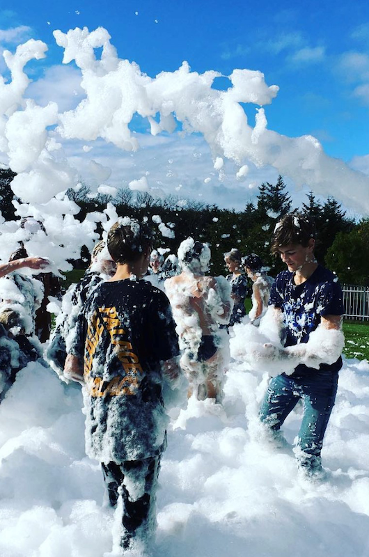 Unge der leger med skum på en græsplæne en skyfri sommerdag